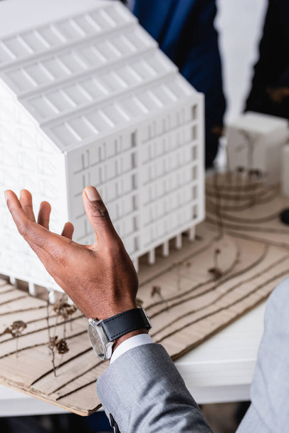 częściowy widok afrykańskiego biznesmena wskazującego ręką na model budynku, zamazane tło - Zdjęcie, obraz