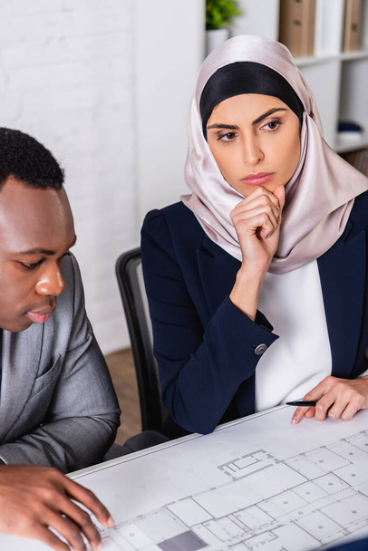 вдумчивая арабская деловая женщина рядом с африканским американским партнером, глядя на план - Фото, изображение