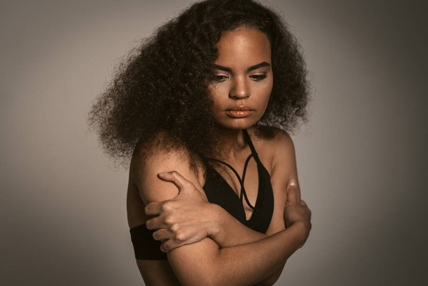 Sensual African American young woman standing covered with hands in black bare shoulder top isolated on grey background. Human emotions, facial expression concept - Foto, Imagen