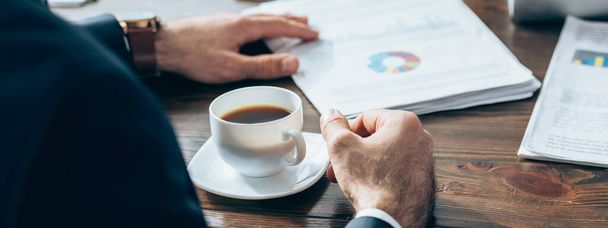 Cropped view of businessman near cup of coffee and papers with charts on blurred background, banner  - Photo, Image