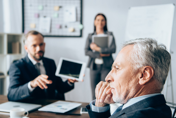 Pensive investor sitting near business people on blurred background in office - Photo, image