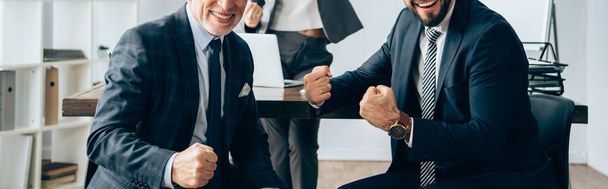 Vista cortada de homem de negócios sorridente mostrando sim gesto perto de empresária em fundo turvo no escritório, banner  - Foto, Imagem