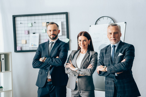 Smiling businesswoman standing with crossed arms near partners in office  - Photo, image