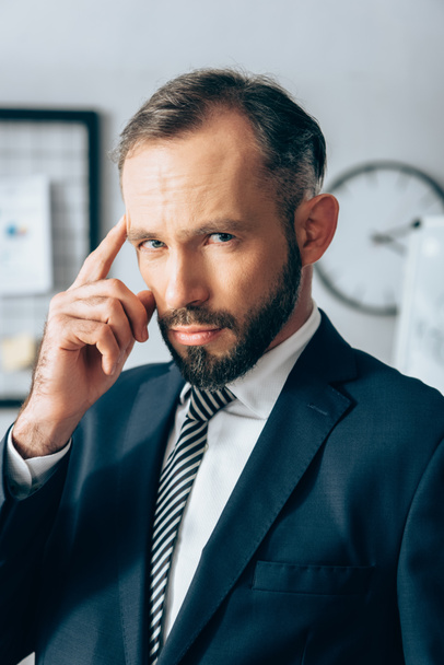 Businessman in formal wear looking at camera and pointing with finger at head in office  - Фото, зображення