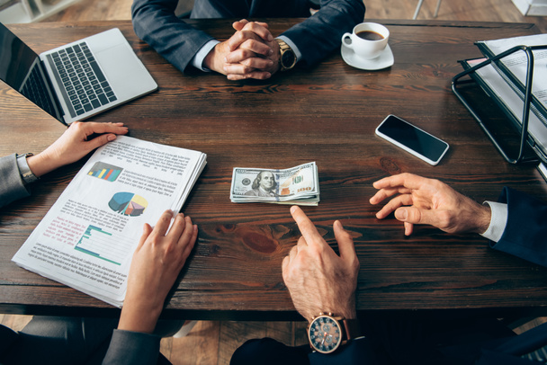 Περικοπή άποψη του επιχειρηματία που δείχνουν προς τα χρήματα κοντά στο συνάδελφο με χαρτιά και συσκευές στο τραπέζι  - Φωτογραφία, εικόνα