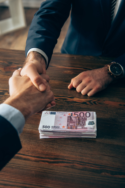 Обрізаний вид бізнесменів тремтячи руками біля євро банкнот на столі
 - Фото, зображення