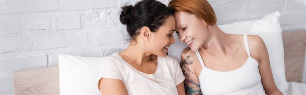 vrolijk interraciaal lesbisch paar lachen gezicht naar gezicht in bed, banner - Foto, afbeelding