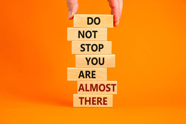 You are almost there symbol. Wooden blocks with words 'do not stop you are almost there'. Male hand. Beautiful orange background, copy space. Business and almost there concept. - Фото, изображение