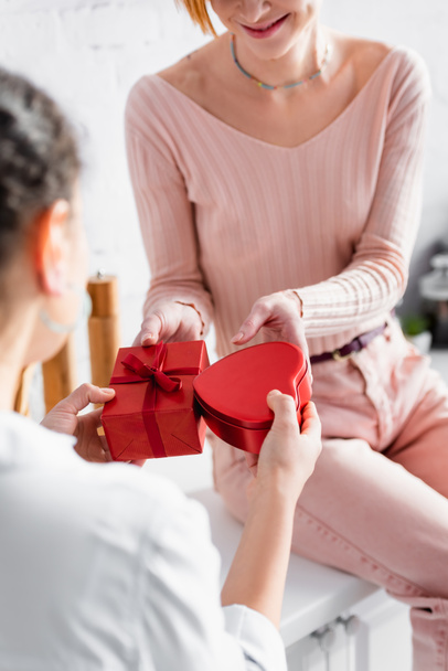 bijgesneden weergave van lesbische vrouw zitten op aanrecht en presenteren geschenken op Valentijnsdag aan vriendin, wazig voorgrond - Foto, afbeelding