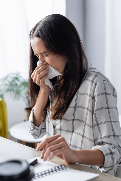 young woman wiping nose with paper napkin while suffering from allergy on blurred foreground - Фото, изображение