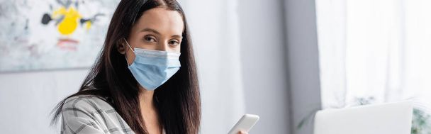 allergic woman in medical mask looking at camera while holding smartphone, banner - Fotó, kép