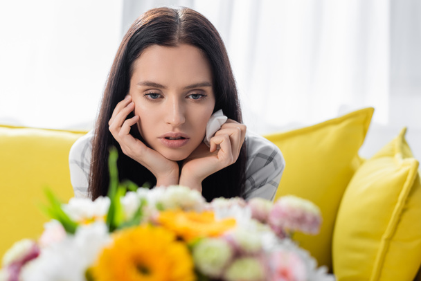 upset allergic woman holding paper napkin near flowers on blurred foreground - Photo, Image