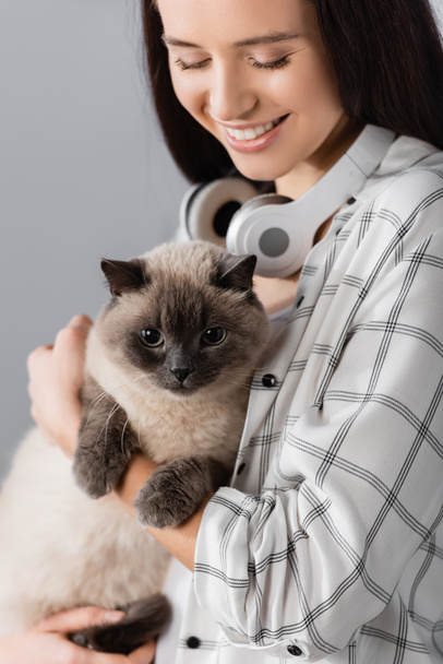 happy woman with wireless headphones on neck holding cat at home - Foto, imagen