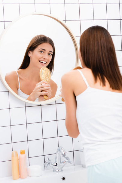 happy young woman singing with hairbrush near mirror in bathroom - Photo, Image
