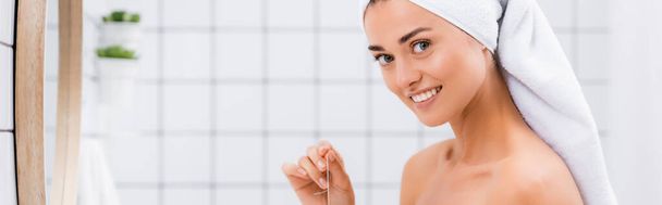 веселая женщина с белым махровым полотенцем на голове, смотрящая в камеру, держа зубную нить, баннер - Фото, изображение