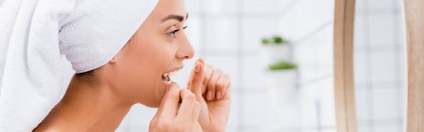 side view of woman with white towel on head flossing teeth near mirror in bathroom, banner - Foto, imagen