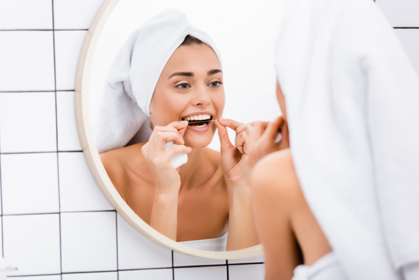 mulher com toalha terry branco na cabeça dentes de limpeza com fio dental no banheiro, foreground borrado - Foto, Imagem