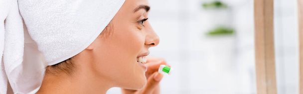 vista lateral de la mujer con toalla blanca en la cabeza sosteniendo el cepillo de dientes en el baño, pancarta - Foto, imagen