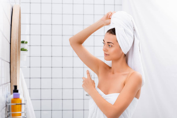 jonge vrouw, verpakt in badstof handdoeken, het aanbrengen van deodorant in de badkamer - Foto, afbeelding