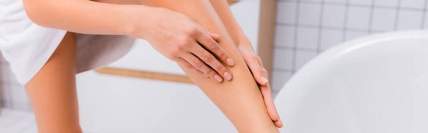 cropped view of woman applying body lotion on leg in bathroom, banner - Фото, зображення