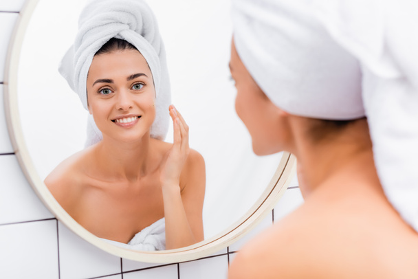 cheerful woman applying facial scrub near mirror in bathroom, blurred foreground - Fotó, kép