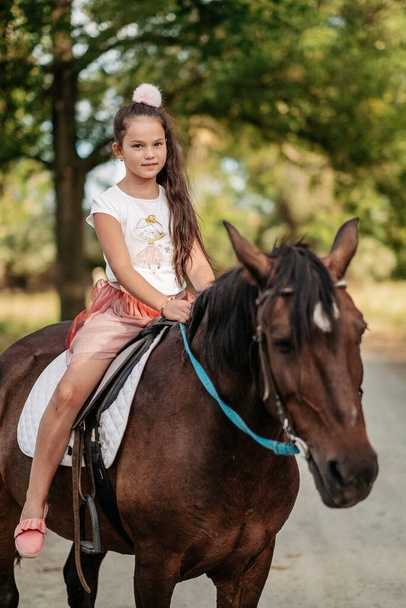Маленька блондинка з довгим волоссям їде на коні в парку на заході сонця восени. Осінній кінь їде. Дружба дівчини і коня
. - Фото, зображення