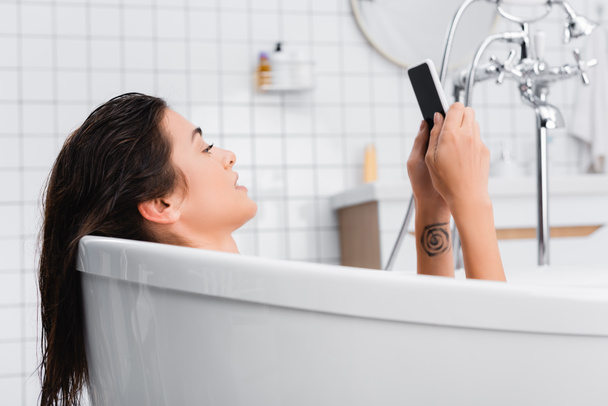 jeune femme tatouée utilisant un smartphone tout en prenant un bain - Photo, image