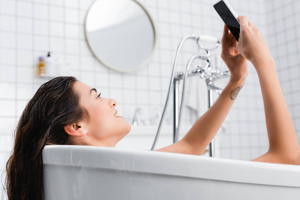 young smiling woman taking selfie while relaxing in bathtub - Zdjęcie, obraz