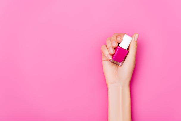 top view of groomed female hand with bottle of glossy nail polish on pink background - Zdjęcie, obraz
