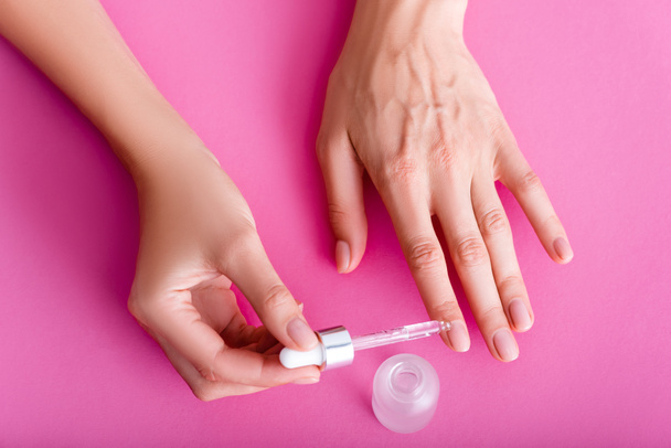 partial view of woman applying cuticle remover with dropper on pink background - Foto, imagen