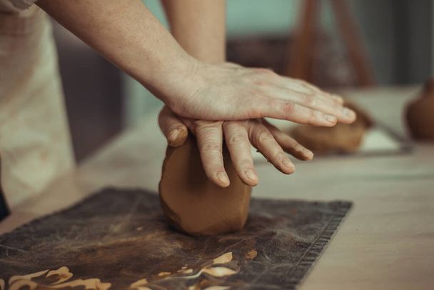 Un uomo stropiccia l'argilla con le mani. Lavora sulla ruota della ceramica. Il padrone sta preparando l'argilla.. - Foto, immagini