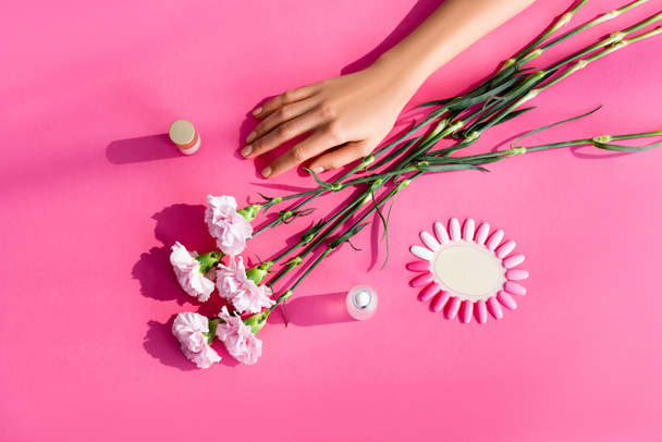 top view of carnation flowers near female hand, palette of artificial nails, nail polish and cuticle remover on pink background - Фото, зображення