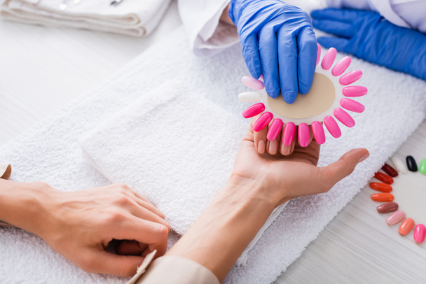 cropped view of manicurist holding palette of artificial nails near hand of client - Photo, Image