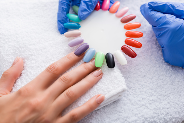 partial view of manicurist holding set of multicolored false nails near hand of client - Photo, Image