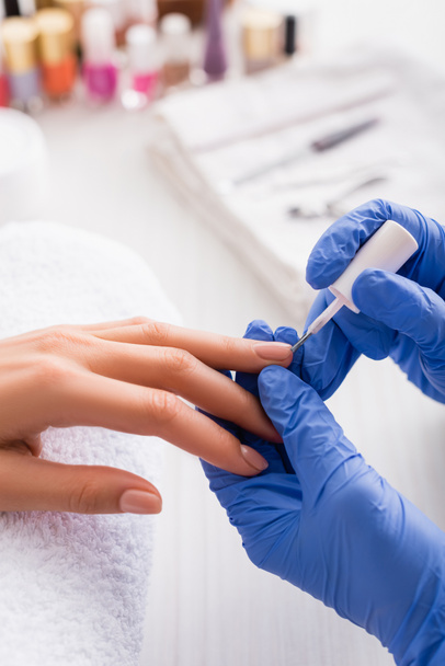 cropped view of manicurist in latex gloves applying nail polish while making manicure to woman - Photo, Image
