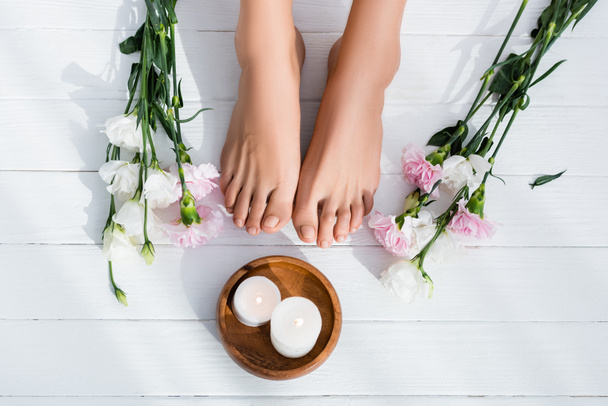top view of groomed female feet, bowl with candles, eustoma and carnation flowers on white wooden surface - Photo, Image