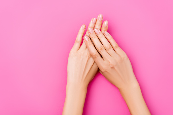 ピンクの背景に光沢のある爪を持つ手入れの行き届いた女性の手のトップビュー - 写真・画像