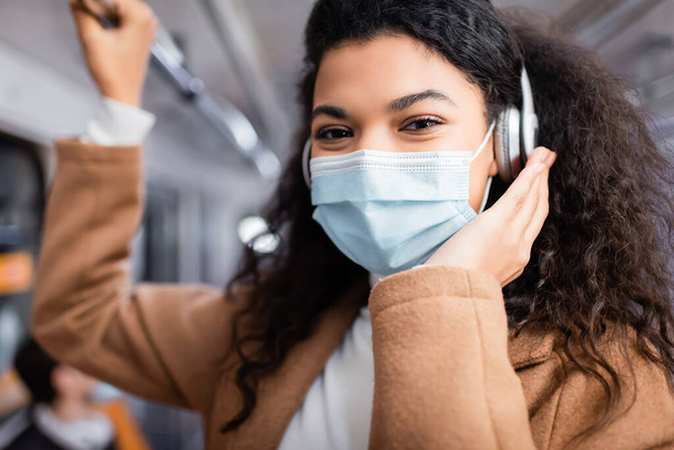 joven afroamericana mujer en máscara médica escuchando música en metro  - Foto, imagen