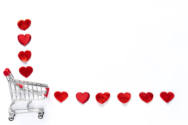 Los pequeños corazones rojos están cayendo de la cesta de la compra en el fondo blanco. - Foto, imagen