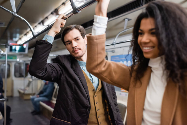 homme regardant femme afro-américaine gaie dans le métro sur le premier plan flou - Photo, image