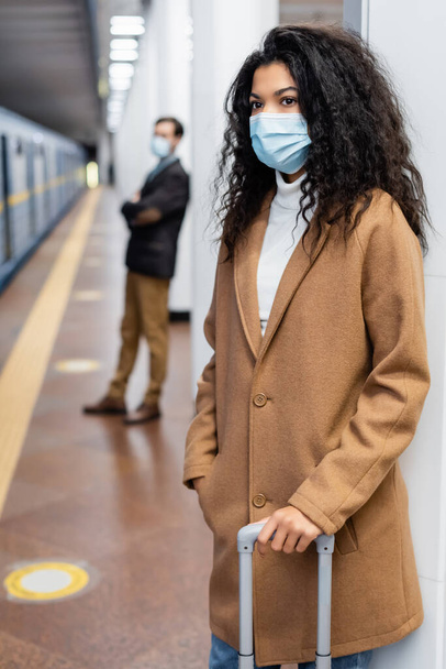 African american woman in medical mask standing with luggage in subway  - Foto, Imagen