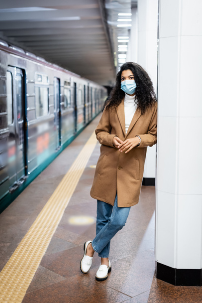 по всей длине кудрявая африканская американка в медицинской маске, стоящая в метро  - Фото, изображение