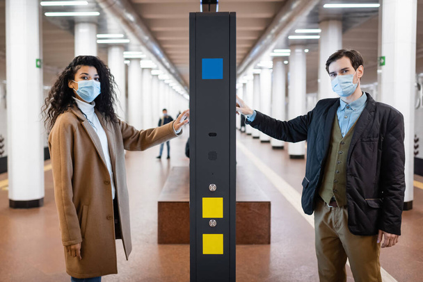 encaracolado Africano americano mulher e homem em máscaras médicas perto de informação stand no metrô - Foto, Imagem