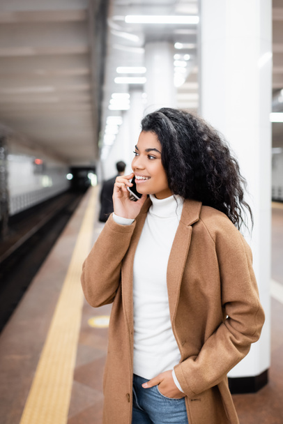 cheerful african american woman talking on smartphone in subway on blurred background  - Photo, Image