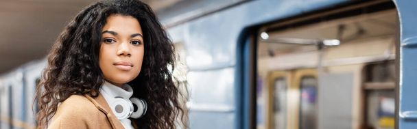 fiatal afro-amerikai nő vezeték nélküli fejhallgató nézi kamera metró, banner - Fotó, kép