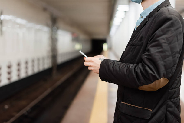 Ausgeschnittener Blick auf tätowierten Mann mit Smartphone in U-Bahn  - Foto, Bild