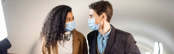 pareja interracial en máscaras médicas mirándose en el metro, pancarta - Foto, Imagen