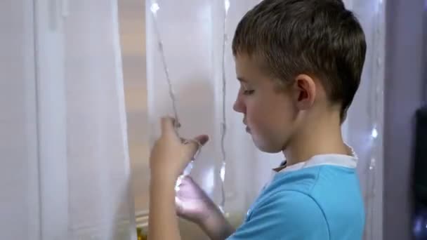 Junge wickelt verworrene Silvestergirlande auf Vorhang auf und steht neben Fenster. - Filmmaterial, Video