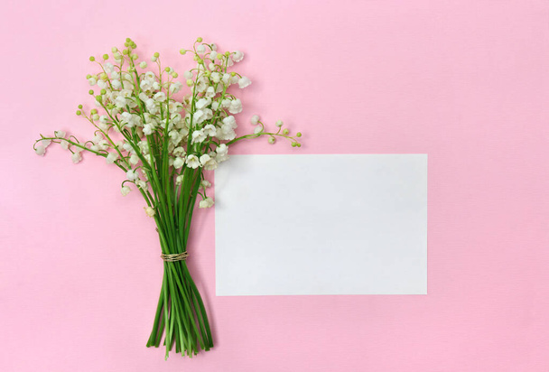 Flores brancas Lírio do vale (Convallaria majalis, sinos de maio, lírio pode) em um fundo de papel rosa com nota de cartão de papel branco com espaço para texto. Vista superior, deitado plano. Decoração Primavera - Foto, Imagem