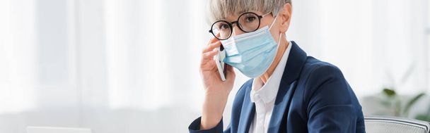 middle aged team leader in glasses and medical mask talking on smartphone, banner - 写真・画像